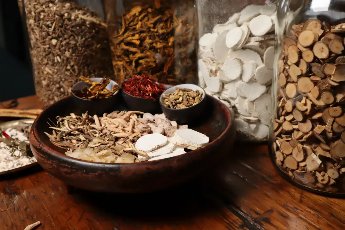 Assorted dried herbs and plant materials displayed in bowls and glass jars on a wooden surface