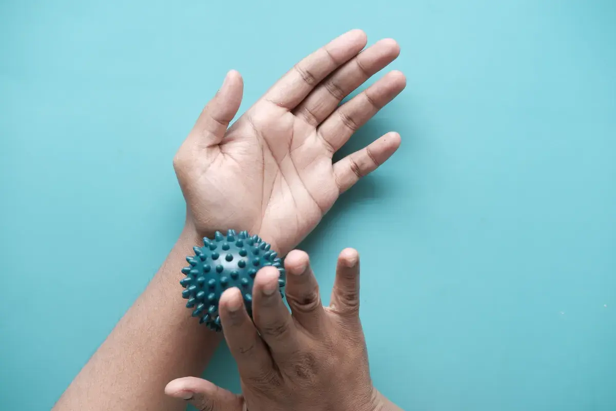 Hands holding a blue spiky massage ball against a light blue background