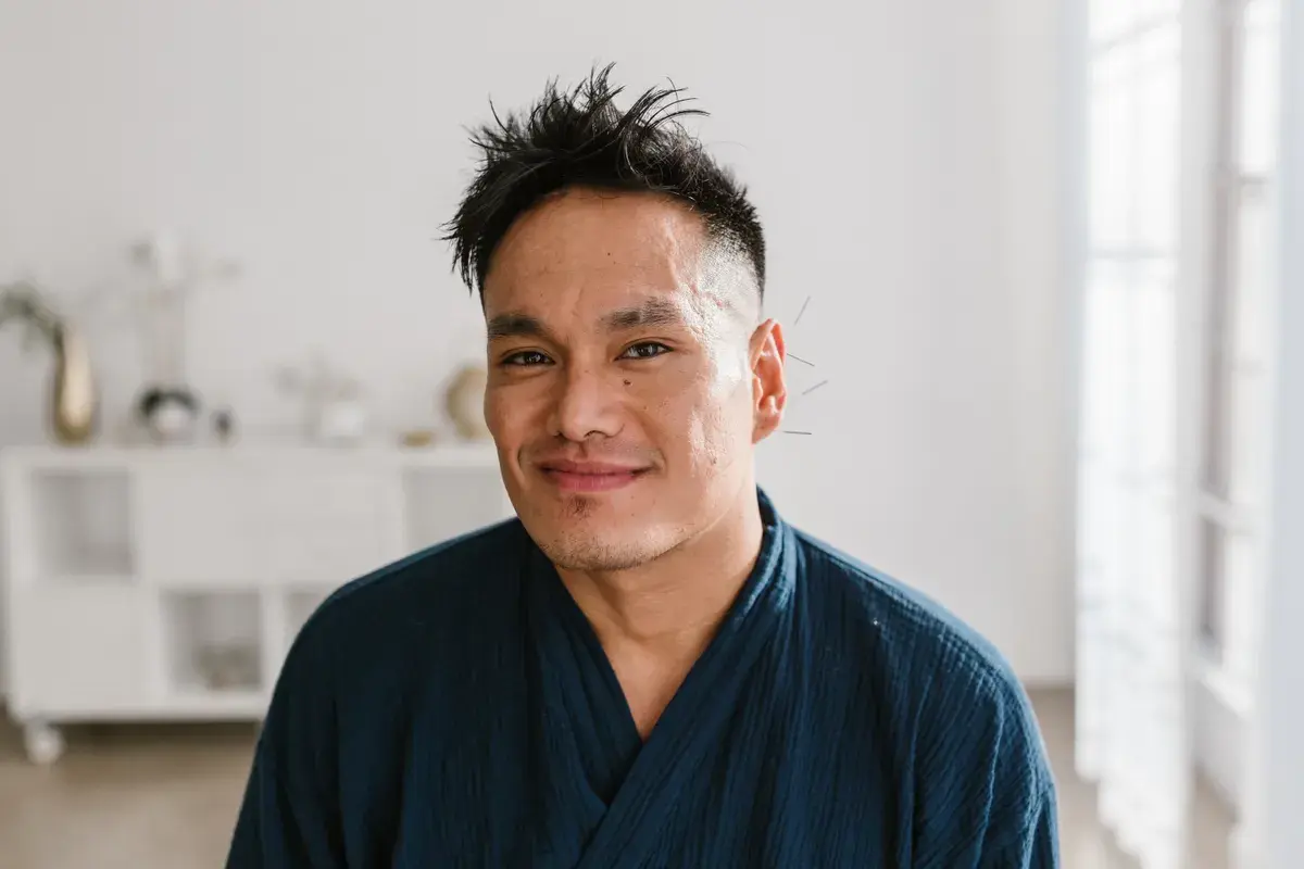 Man with acupuncture needles in his ear, smiling at the camera in a bright indoor space