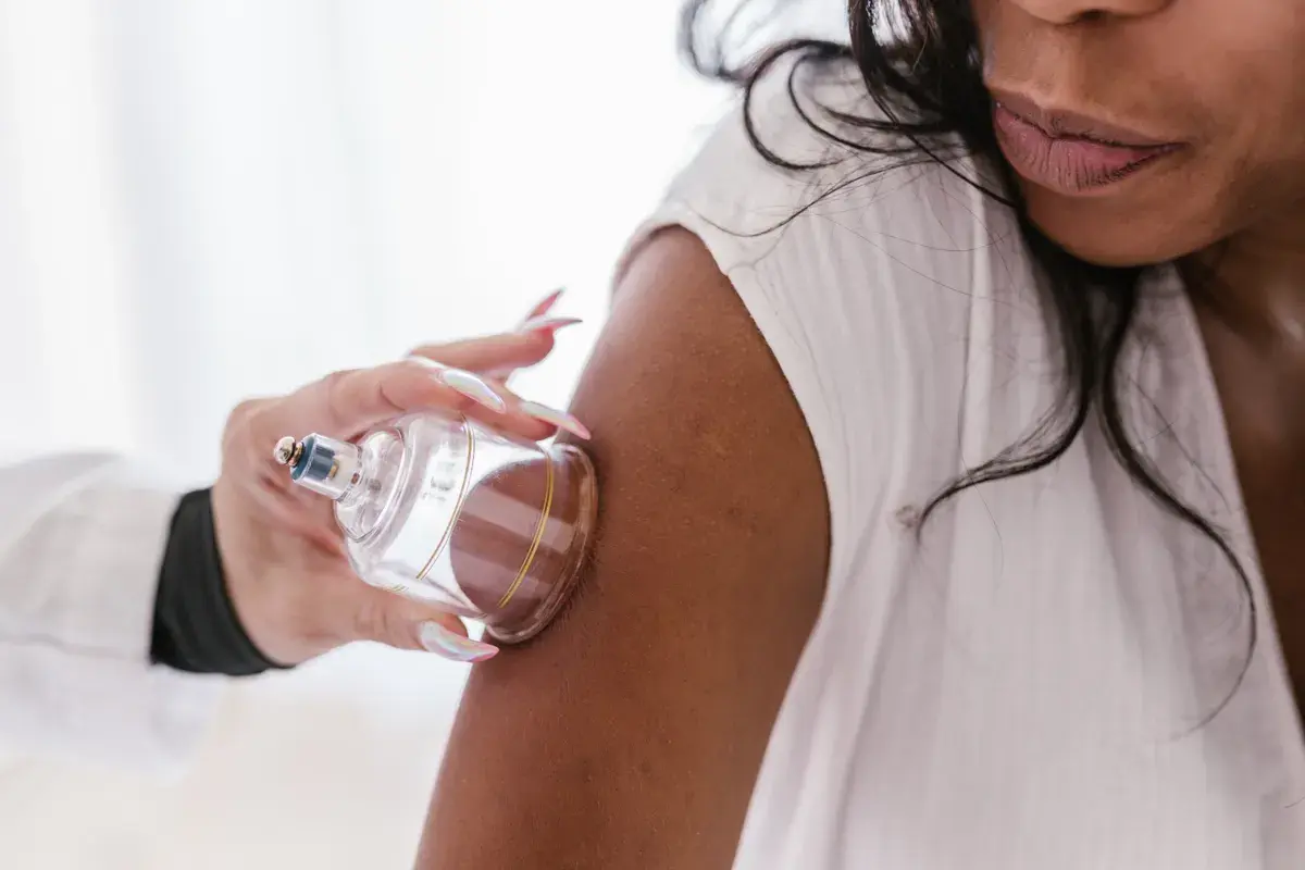 Woman holding a clear glass perfume bottle against her arm