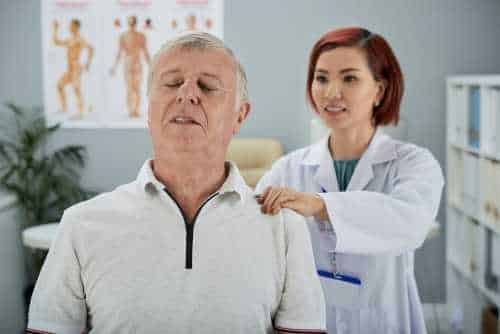 Practitioner examining an older man’s shoulders