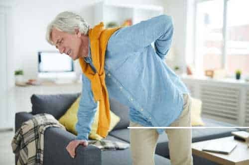 Older man holding his lower back as he stands up from a sofa