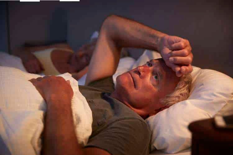 Older man awake in bed with a hand on his forehead