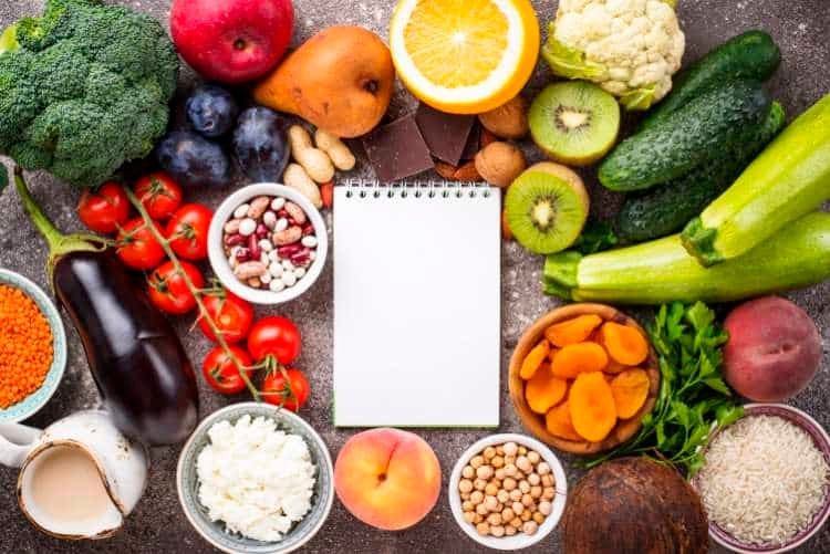Fresh vegetables, fruit, grains and a notepad on a table