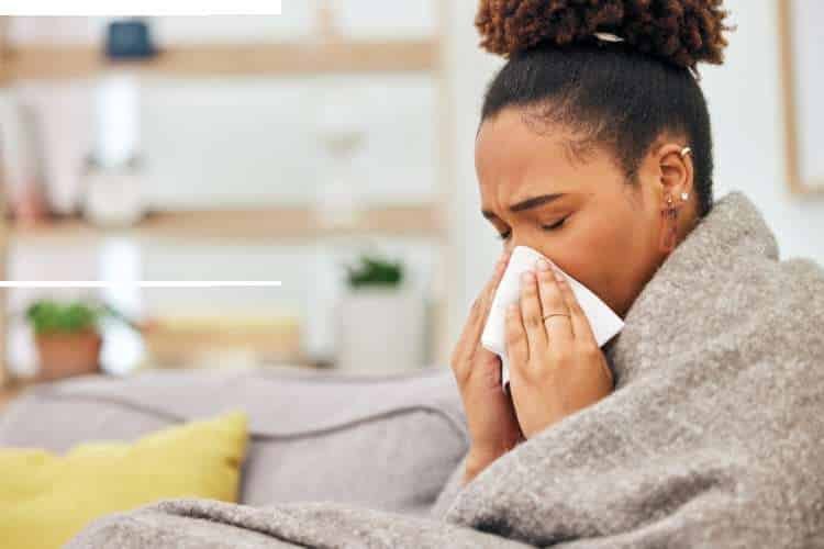 Woman blowing her nose, wrapped in a blanket